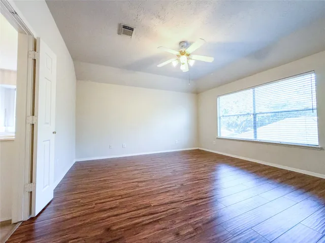 an empty room with wooden floor chandelier fan and windows