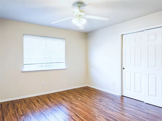 an empty room with wooden floor chandelier fan and windows