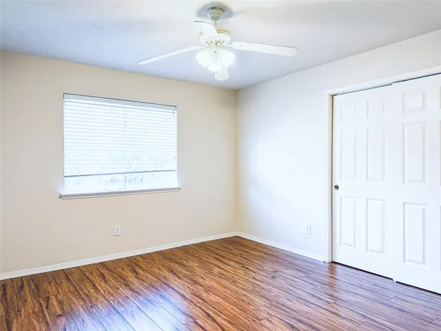 an empty room with wooden floor chandelier fan and windows