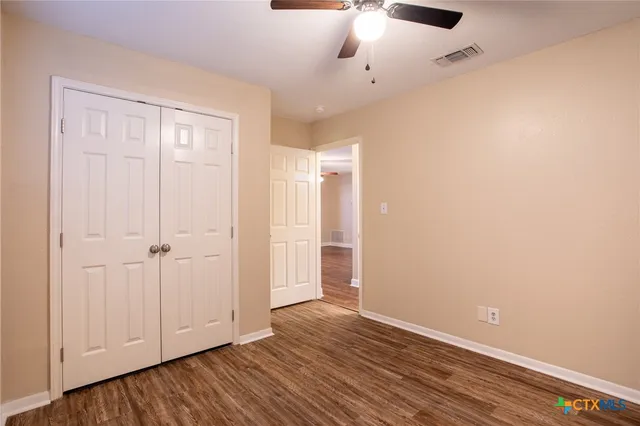 an empty room with wooden floor chandelier fan and windows