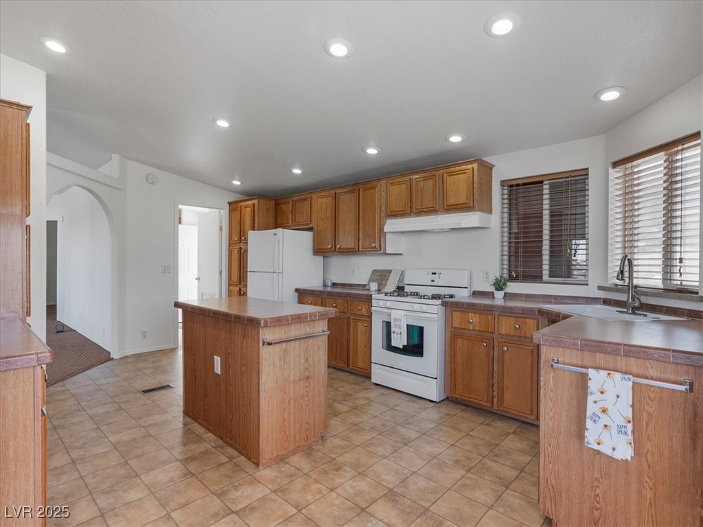 70 West Bonanza Road Las Vegas, NV 89124 - Photo 21 of 71 Kitchen with white appliances, a sink, a center island, arched walkways, and brown cabinetry