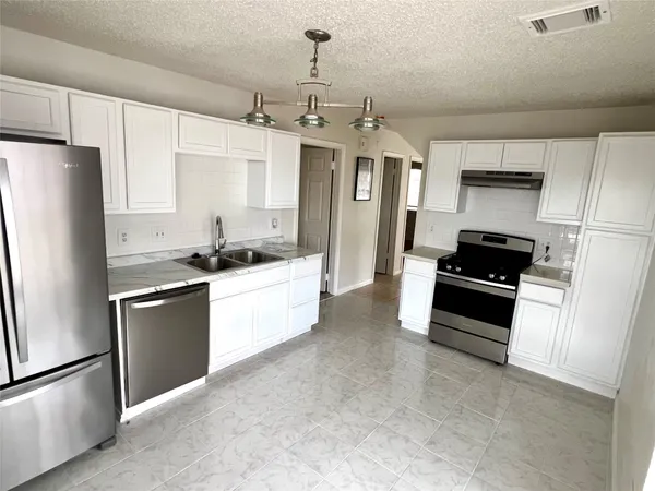 a kitchen with stainless steel appliances kitchen island granite countertop a refrigerator a sink a stove and white cabinets