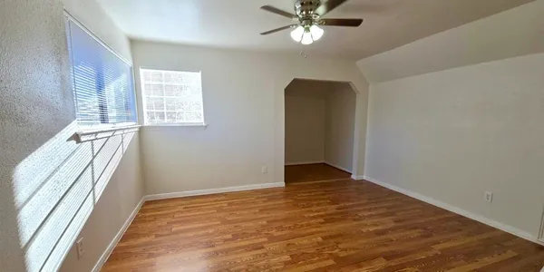 an empty room with wooden floor fan and windows