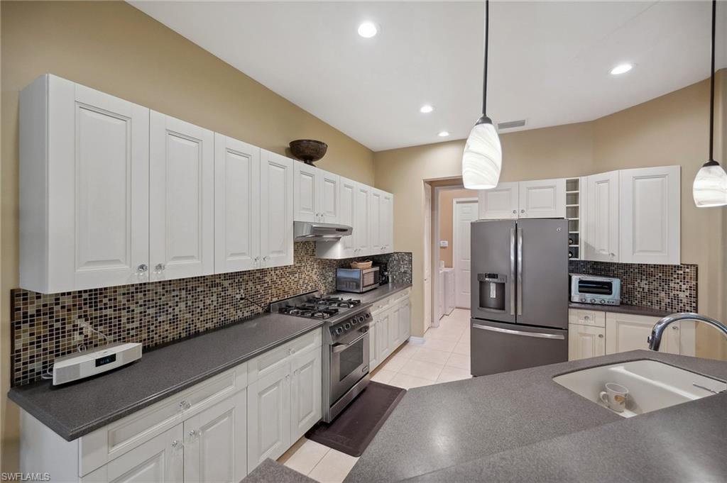 10748 Fieldfair Drive Naples, FL 34119 - Photo 11 of 36 a kitchen with granite countertop a refrigerator a sink and white cabinets
