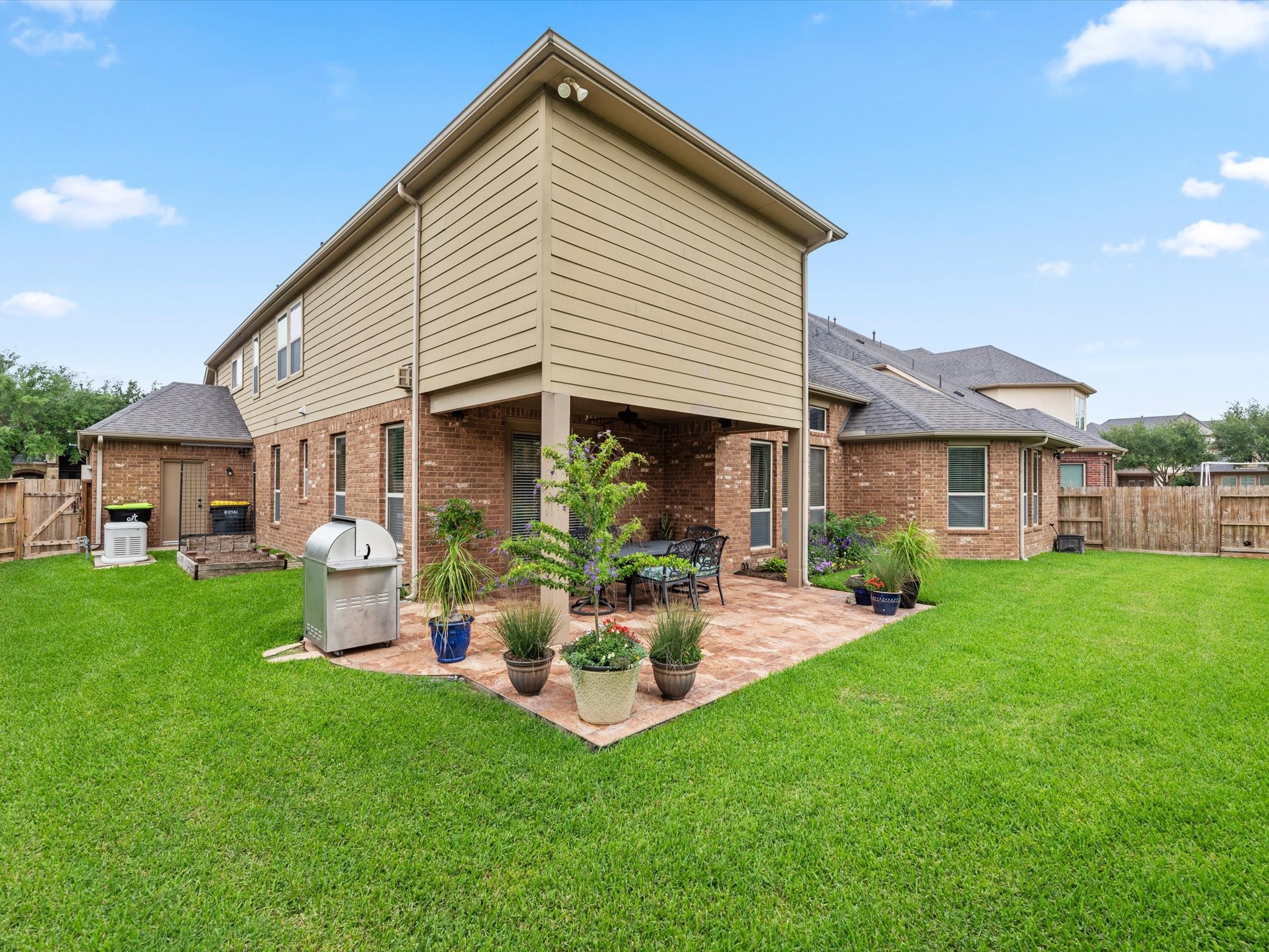 3907 Randle Ridge Court Fulshear, TX 77441 - Photo 41 of 46 This photo showcases a spacious backyard featuring a well-maintained lawn, a covered patio with ample seating areas. The brick exterior of the house adds charm, and there's room for the grill and for outdoor cooking. Ideal for entertaining and relaxation.