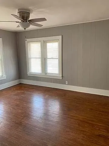 an empty room with wooden floor fan and windows
