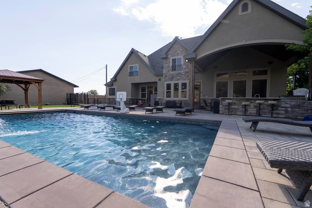 687 South 2080th Street East Springville, UT 84663 - Photo 101 of 149 Expansive backyard oasis featuring a substantial swimming pool with a water feature, extensive paver patio surround, a stone-clad outdoor kitchen with bar seating, and a covered patio area