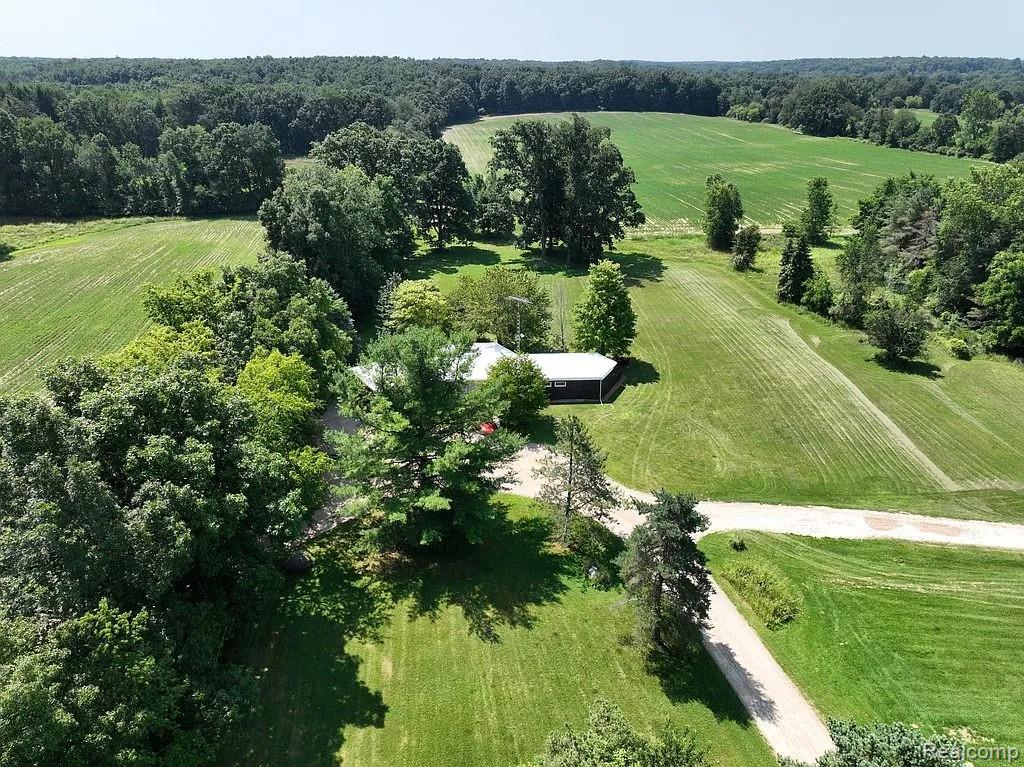 7386 Dean Road Fenton, MI 48430 - Photo 8 of 64 Expansive green fields, mature trees, gravel driveways, and a single-story structure with a light-colored roof