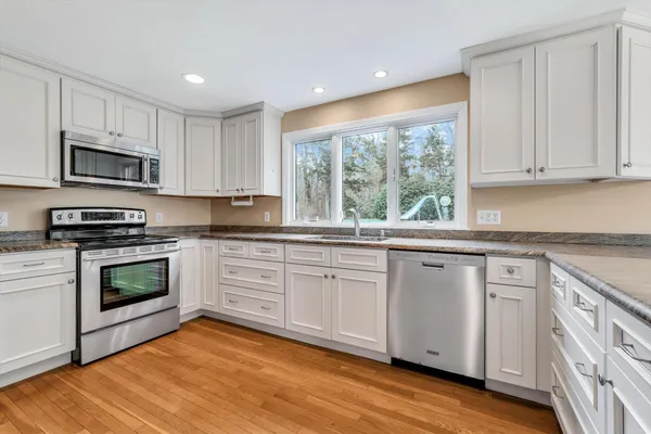 a kitchen with granite countertop white cabinets stainless steel appliances and wooden floor