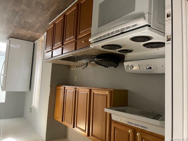Kitchen with stove, white refrigerator, brown cabinetry, extractor fan, and dark wood-type flooring