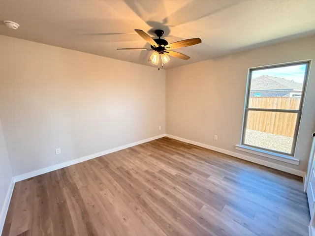 an empty room with wooden floor fan and windows