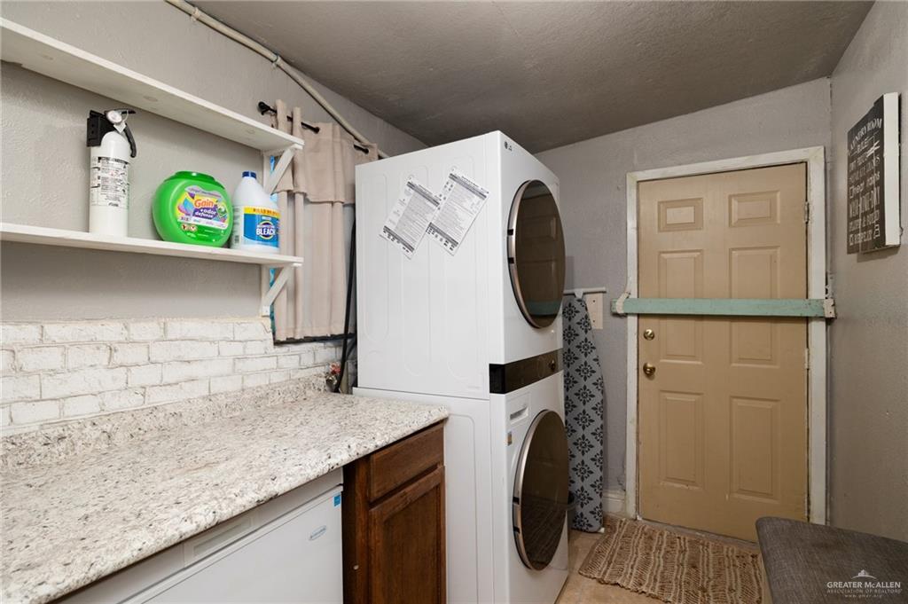 411 East 4th Street Rio Grande City, TX 78582 - Photo 11 of 12 Laundry area featuring a stacked washer and dryer unit, a countertop with a brick-style backsplash, and open shelving