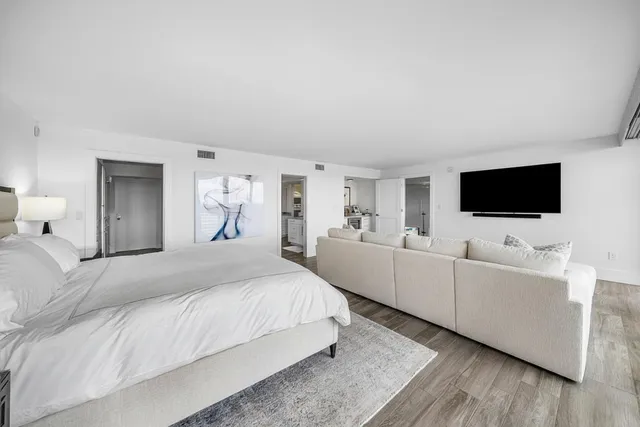 a spacious bedroom with a bed and a flat tv screen on dresser