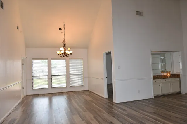 an empty room with wooden floor chandelier and windows