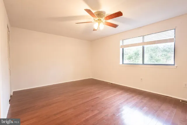 an empty room with wooden floor fan and windows
