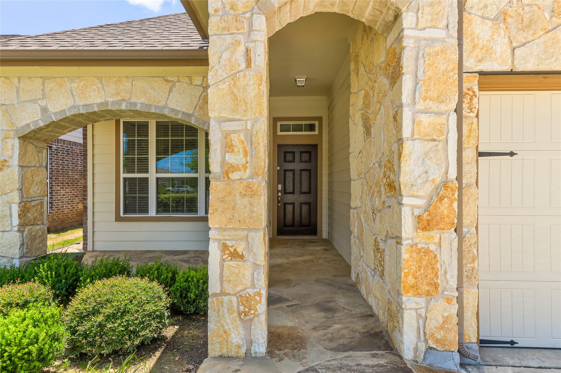 205 Penna Lane Georgetown, TX 78628 - Photo 2 of 32 A welcoming stone archway leads to the dark entry door, framed by vibrant green shrubs and a garage door.