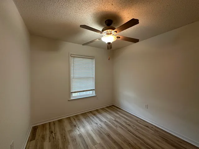 an empty room with wooden floor fan and windows