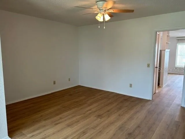 an empty room with wooden floor fan and windows