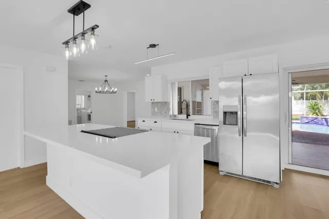 a large white kitchen with a refrigerator a sink dishwasher a stove and a dining table with wooden floor