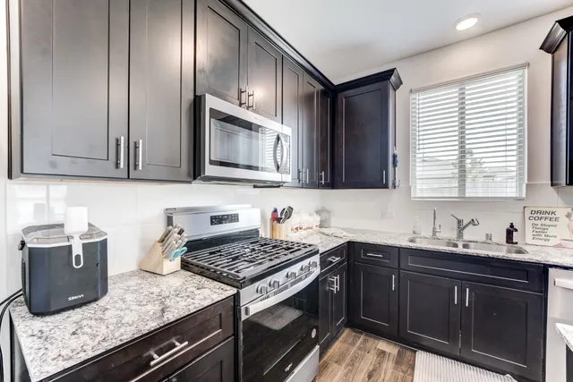 a kitchen with stainless steel appliances granite countertop a sink dishwasher a stove a refrigerator with a dining table and chairs