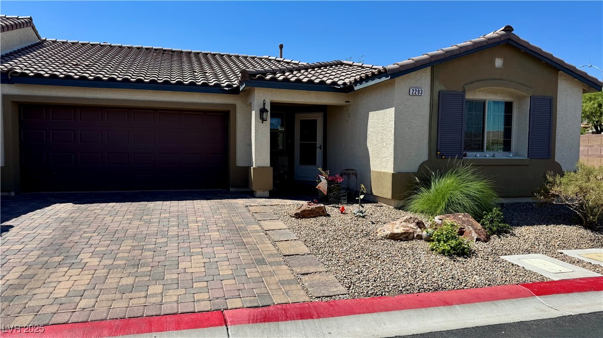 View of front of home featuring decorative driveway, stucco siding, and an attached garage