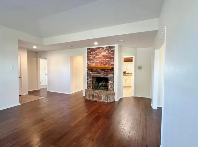 a view of an empty room with wooden floor fireplace and a window