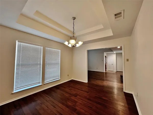 an empty room with wooden floor chandelier and windows