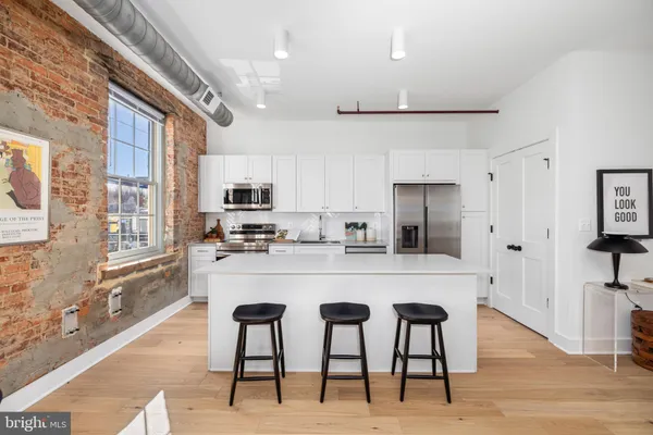 a kitchen with stainless steel appliances kitchen island granite countertop a refrigerator a stove a sink a dining table and chairs with wooden floor