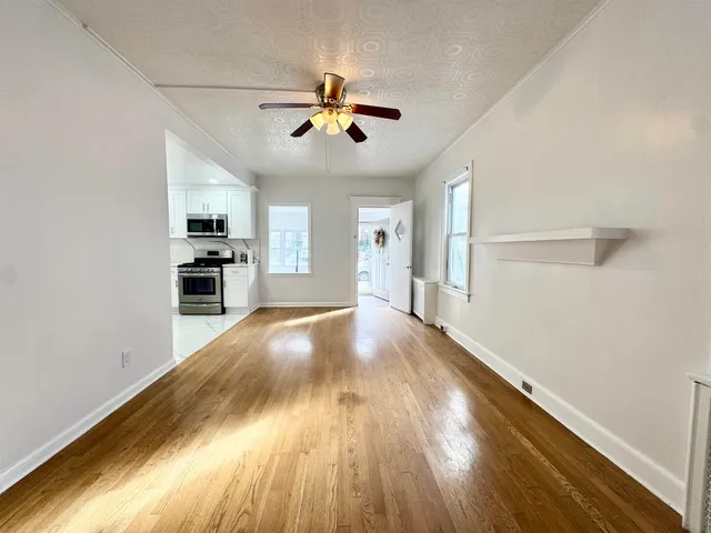 a view of a livingroom with wooden floor a ceiling fan and kitchen space