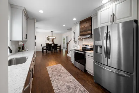 a kitchen with stainless steel appliances granite countertop a refrigerator a stove a sink a dining table and chairs with wooden floor