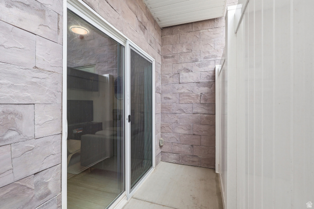 2085 North Main Street, Unit 104 Sunset, UT 84015 - Photo 3 of 19 Outdoor patio space featuring textured stone-look wall panels, a white vinyl privacy fence, and a white sliding glass door with a screen