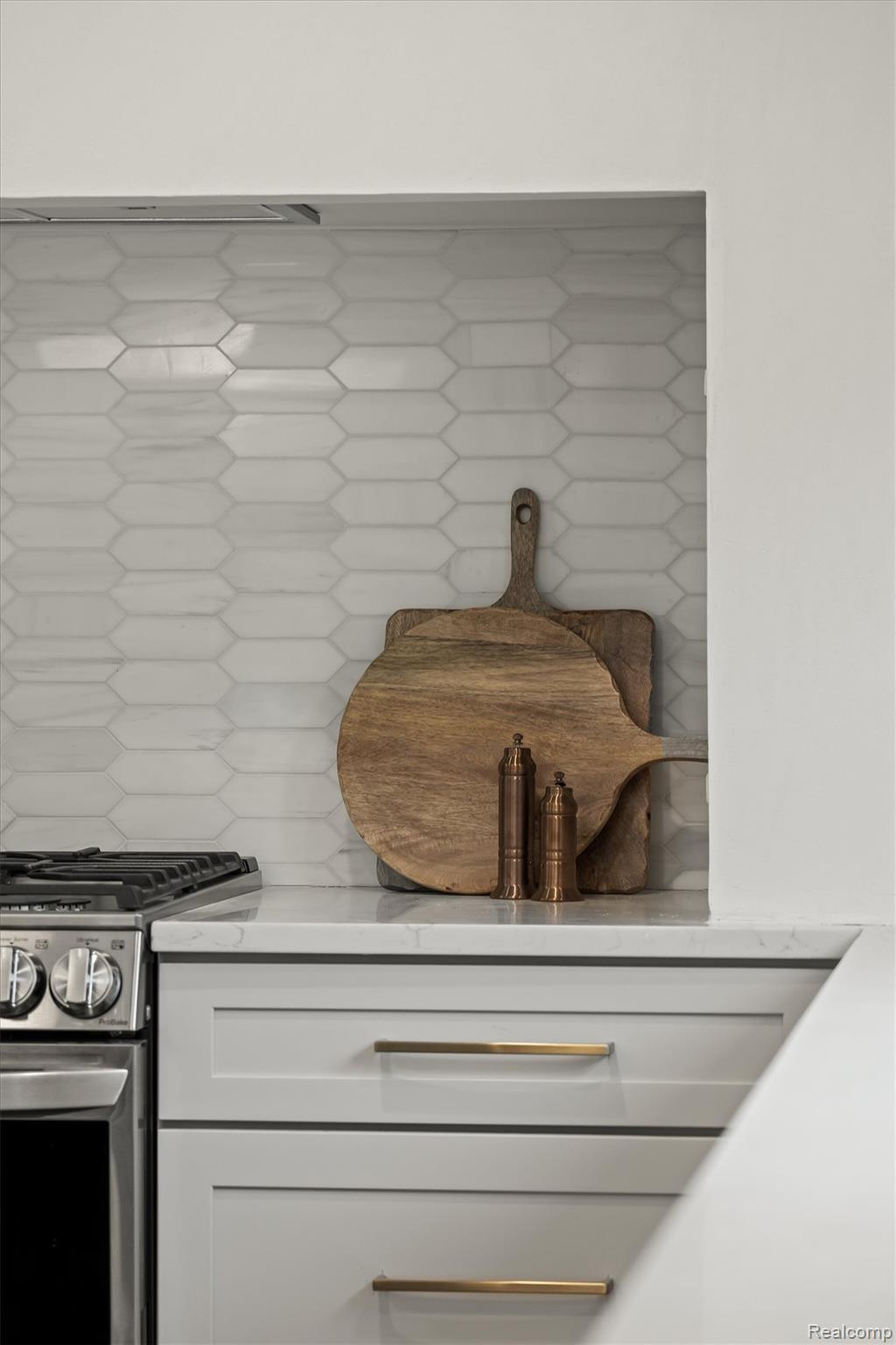 347 Highland Avenue Rochester, MI 48307 - Photo 15 of 59 White picket tile backsplash with a subtle geometric pattern, stainless steel gas range, light-toned countertop, and white shaker-style cabinetry with gold-tone hardware