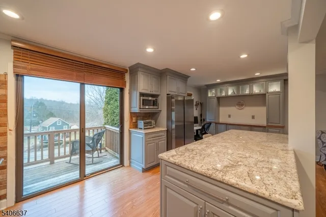 a kitchen with stainless steel appliances kitchen island granite countertop a refrigerator a oven a sink and wooden cabinets with wooden floor