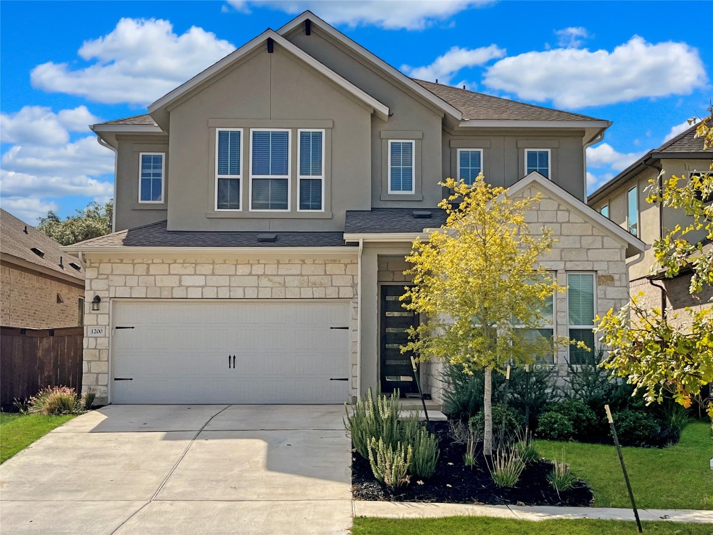 View of front of house featuring stone siding, roof with shingles, and driveway