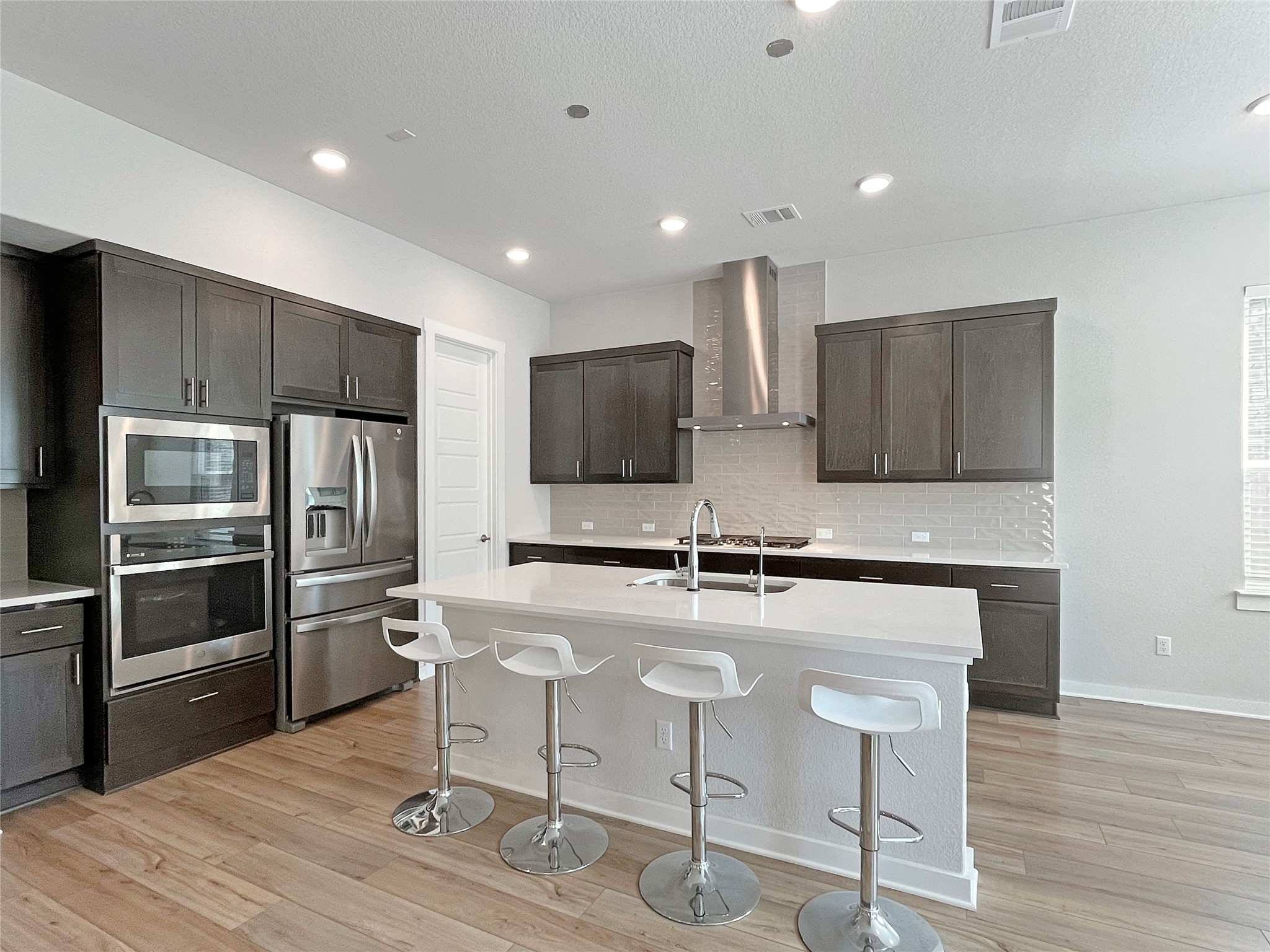 1200 Willie Rnch Way Leander, TX 78641 - Photo 2 of 25 Kitchen with appliances with stainless steel finishes, a kitchen bar, tasteful backsplash, dark brown cabinetry, and light wood-type flooring