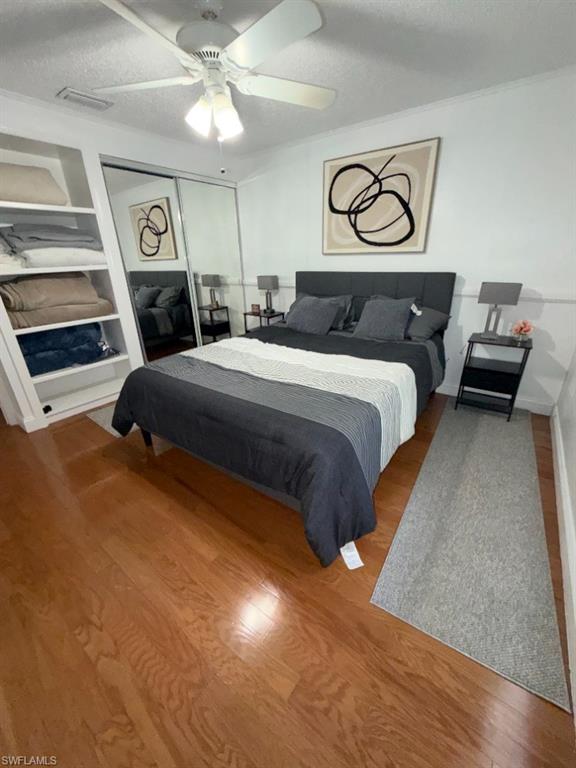 5395 Treetops Drive, Unit I Naples, FL 34113 - Photo 15 of 18 Bedroom featuring wood-finish flooring, built-in shelving, mirrored closet doors, a white ceiling fan with integrated lighting, and crown molding