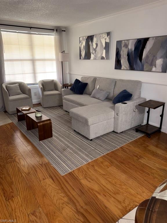 5395 Treetops Drive, Unit I Naples, FL 34113 - Photo 8 of 18 Living area featuring wood flooring, neutral wall tones, white crown molding, and a large window with blinds and sheer curtains