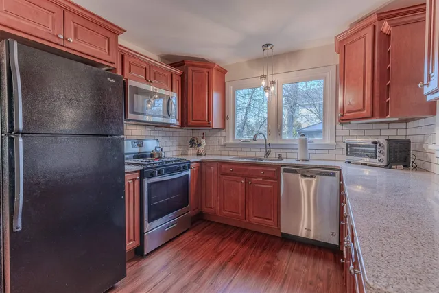 a kitchen with stainless steel appliances granite countertop a refrigerator a sink dishwasher a stove top oven a large island with wooden floor and cabinets