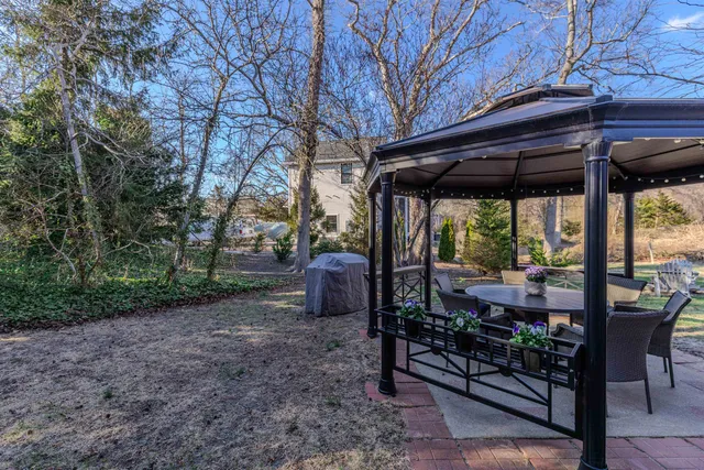 a view of a patio with table and chairs under an umbrella with large trees