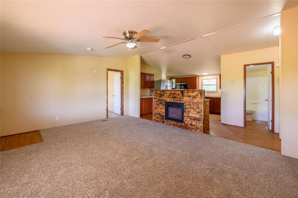 383 Soaring Eagle Trail Wichita Falls, TX 76310 - Photo 11 of 36 Unfurnished living room featuring vaulted ceiling, light colored carpet, ceiling fan, and a fireplace
