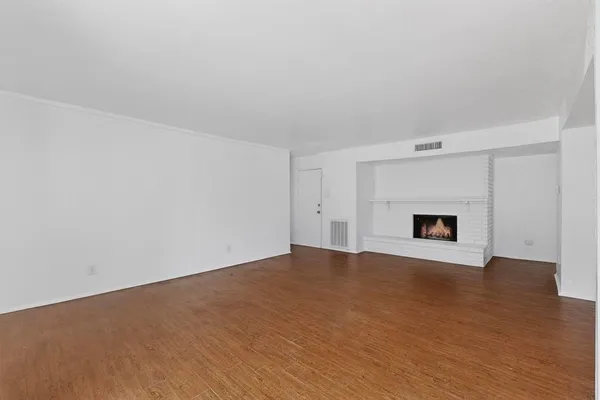 a view of an empty room with wooden floor and a fireplace