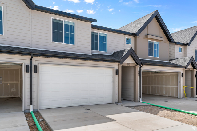1907 East 640th North, Unit 1225 Salem, UT 84653 - Photo 1 of 20 Contemporary townhome exterior featuring light beige siding, dark-trimmed pitched roofs, white garage doors, and black exterior lighting fixtures