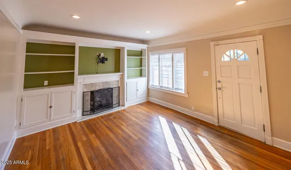 a view of an empty room with wooden floor fireplace and a window
