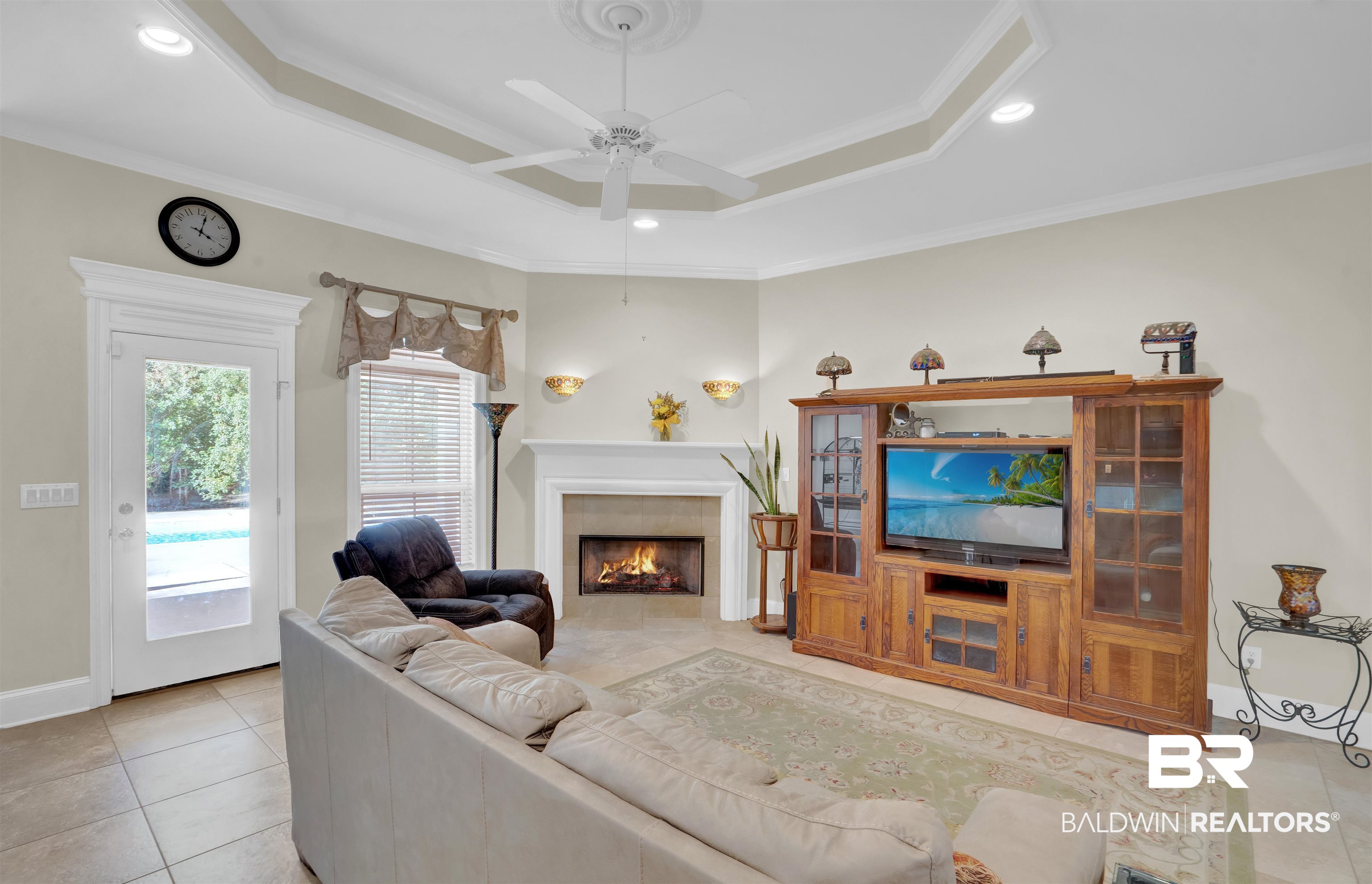 10951 Driver Court Fairhope, AL 36532 - Photo 18 of 46 Tiled living room with a tiled fireplace, ceiling fan, a tray ceiling, and crown molding