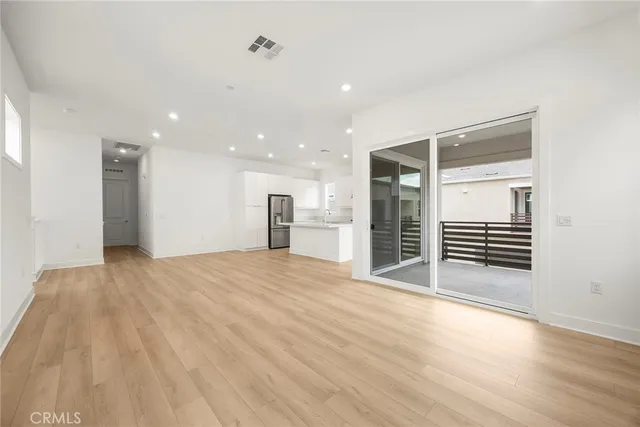 a view of an empty room with wooden floor and a kitchen