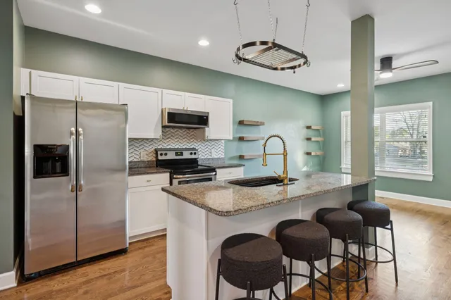 a kitchen with stainless steel appliances granite countertop a refrigerator a sink a stove and chairs with wooden floor