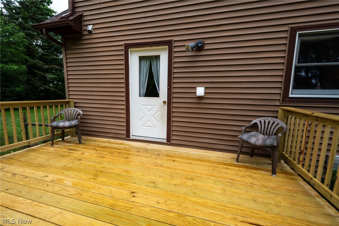 14027 Mayfield Road Huntsburg, OH 44046 - Photo 41 of 50 Spacious wooden deck featuring a white exterior door with window, brown siding, a brown gutter system, and an exterior light fixture