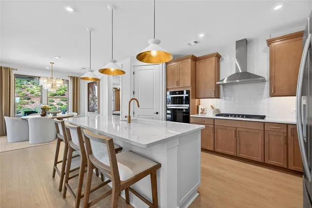 a kitchen with stainless steel appliances granite countertop a stove a sink a oven a dining table and chairs with wooden floor