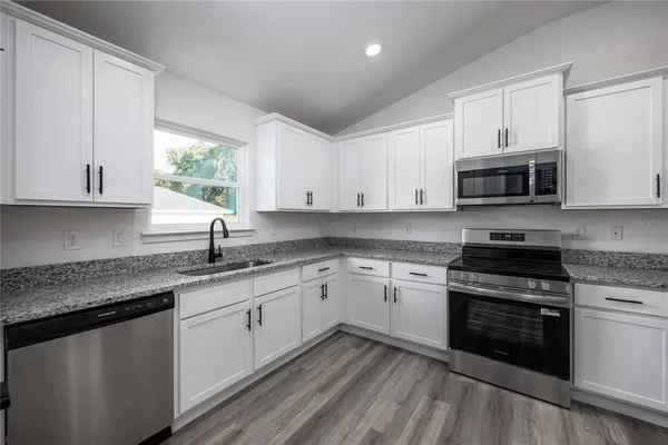 a kitchen with granite countertop white cabinets appliances a window and a sink