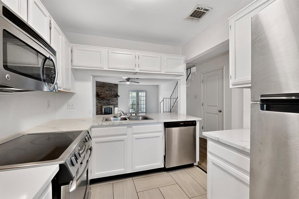 46 Abbey Road Euless, TX 76039 - Photo 5 of 16 Kitchen with stainless steel appliances, white cabinets, ceiling fan, a peninsula, and light stone counters